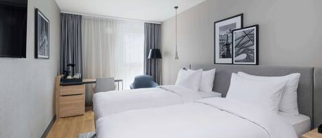 Habitación de hotel con dos camas, un escritorio, una silla y obras de arte en las paredes.