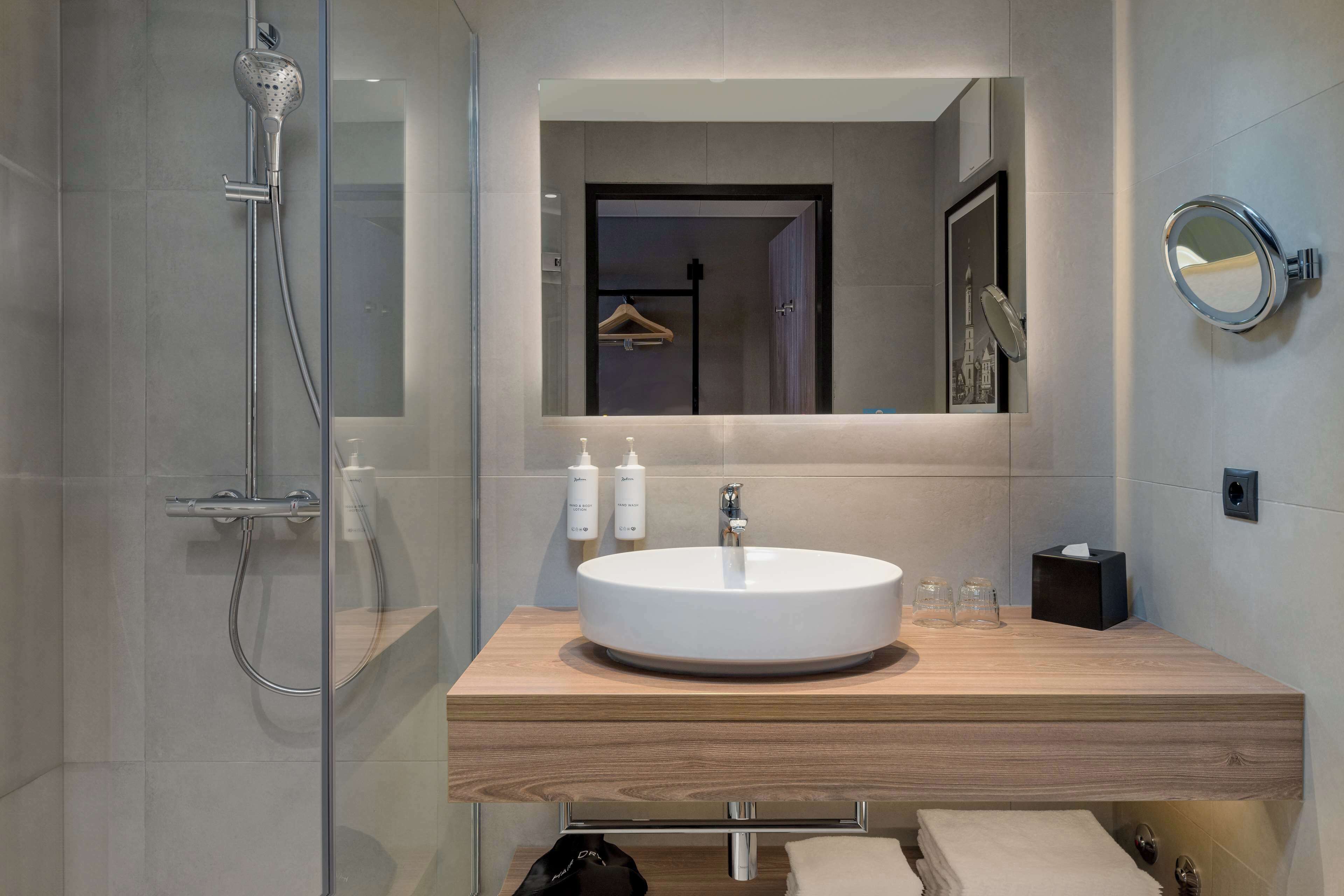 A modern bathroom with a glass-enclosed shower, a round sink, and a mirror.