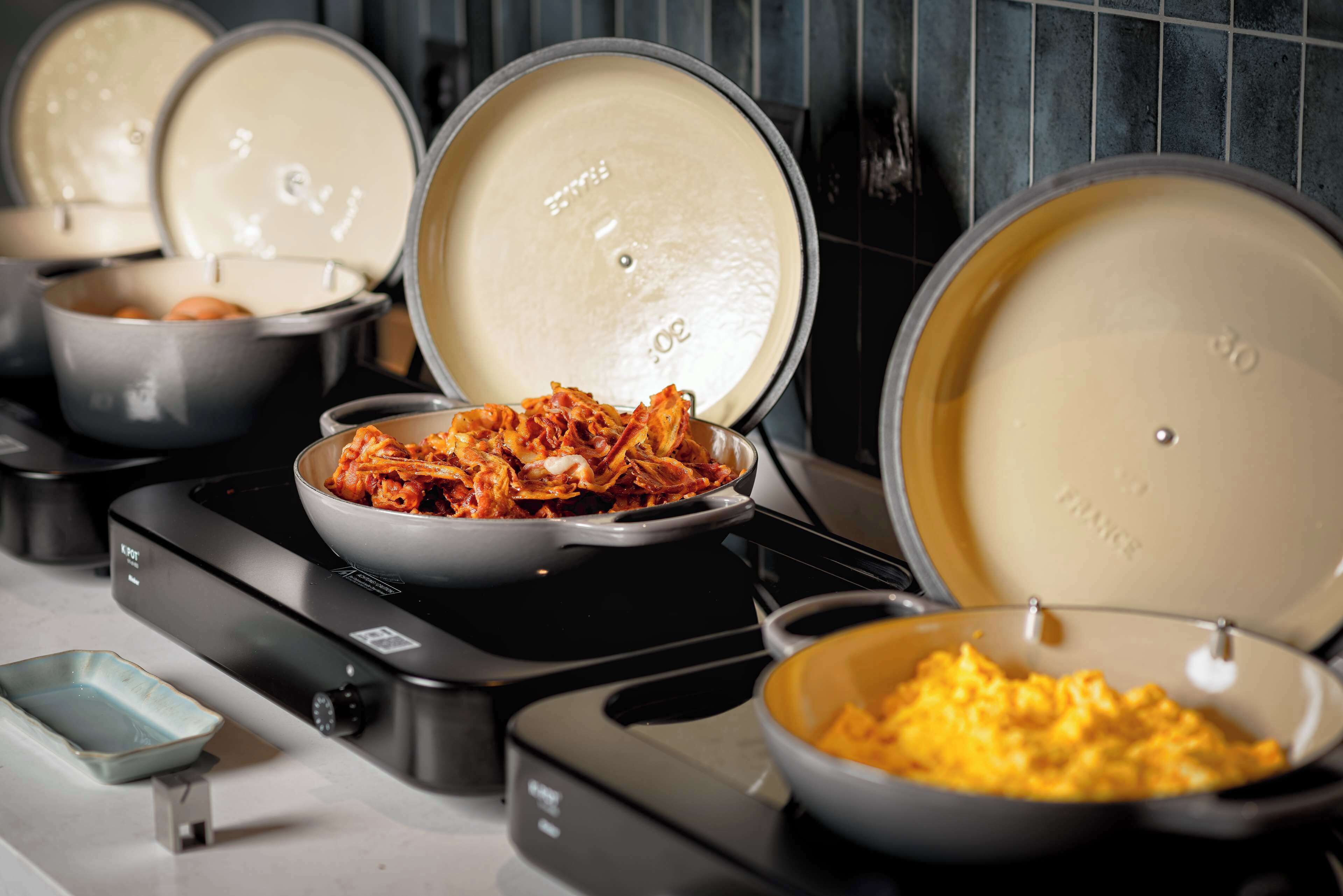 Uma cozinha com várias panelas no fogão, incluindo uma tigela de ovos mexidos e um prato de kimchi.