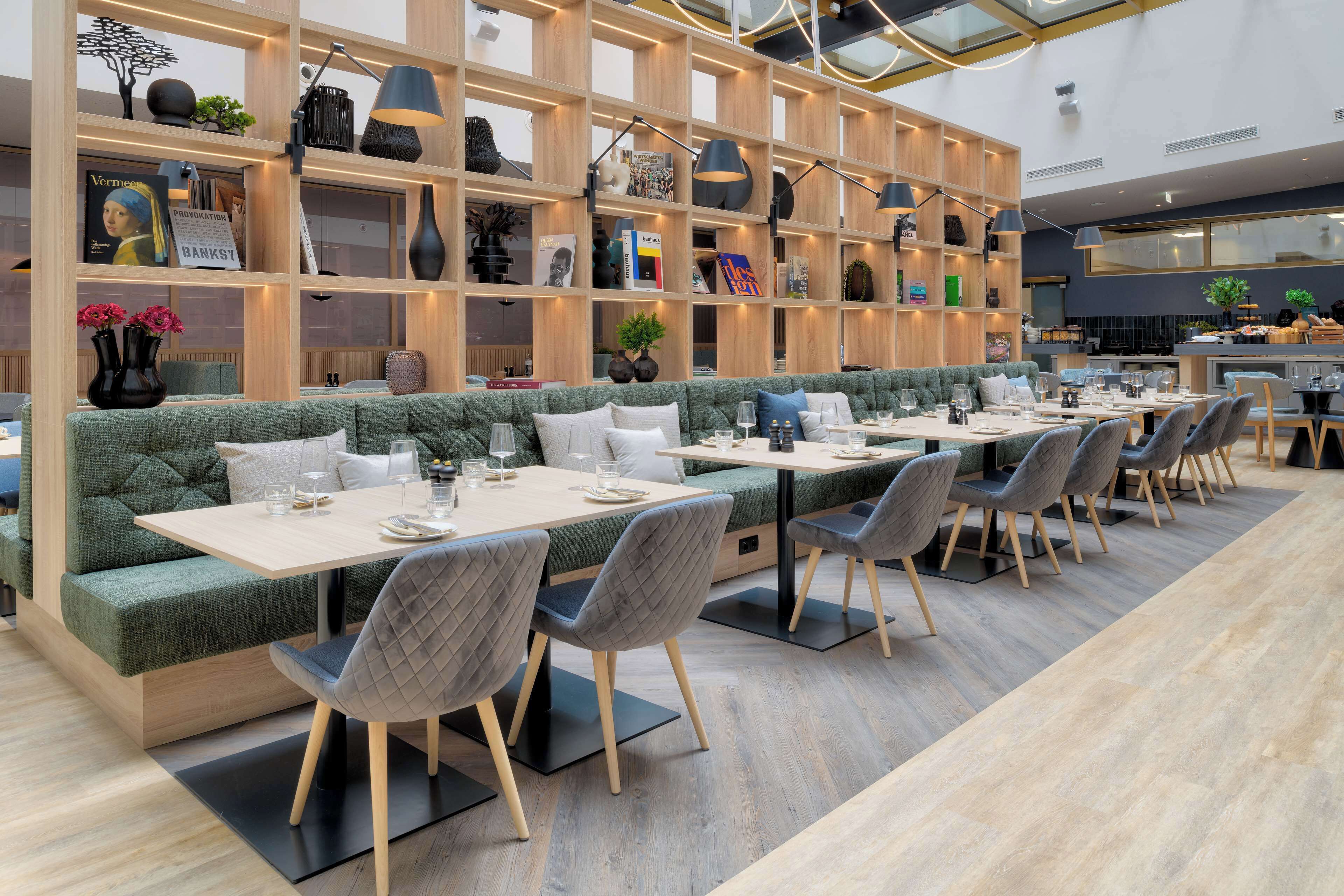 A modern restaurant with a long dining area, cushioned seating, and a variety of books and decorative items on shelves.