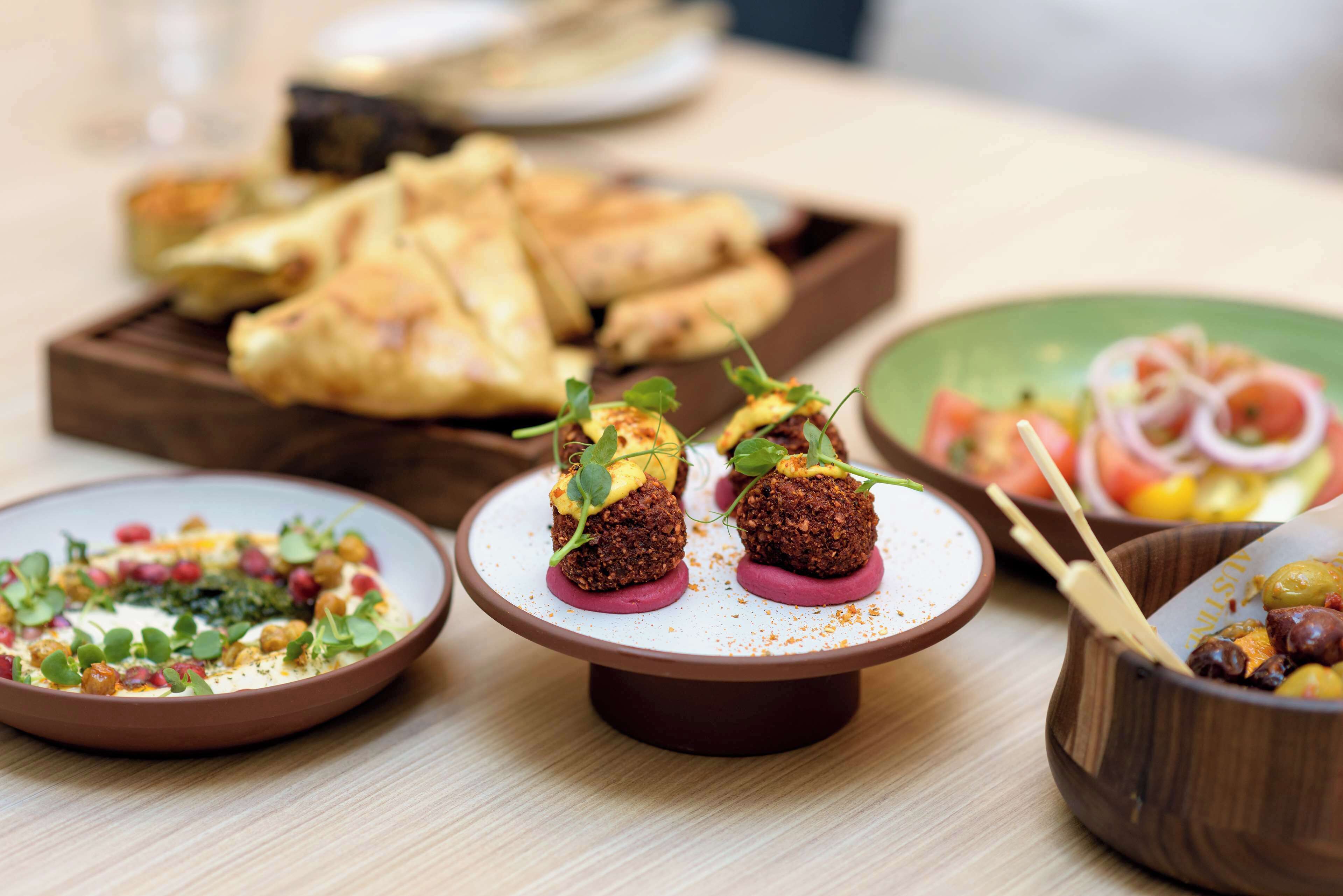 Variedad de platos en una mesa, incluyendo un plato con dos albóndigas cubiertas de verduras y un bol de aceitunas.