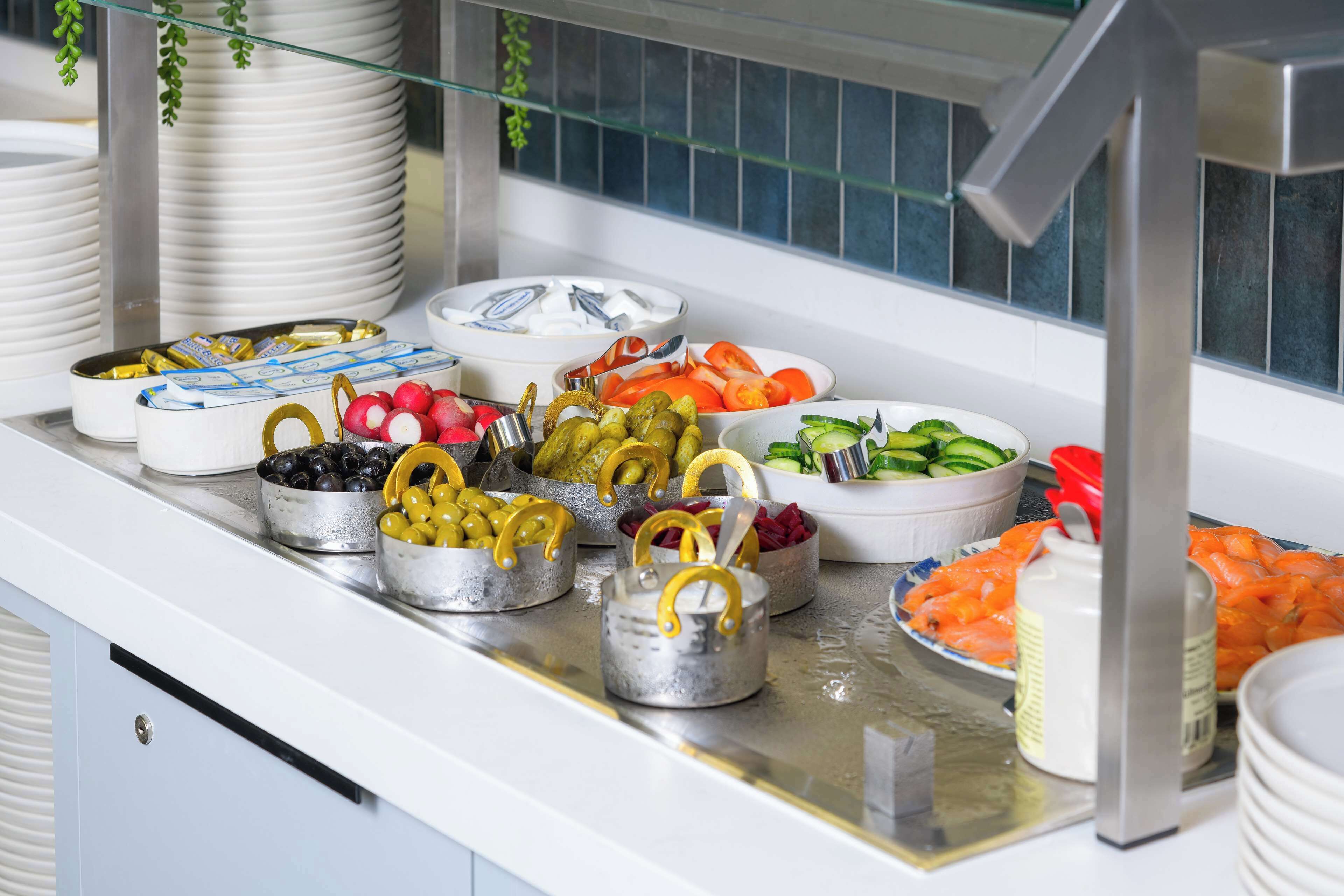 A buffet with various food items including olives, tomatoes, cucumbers, and salmon.