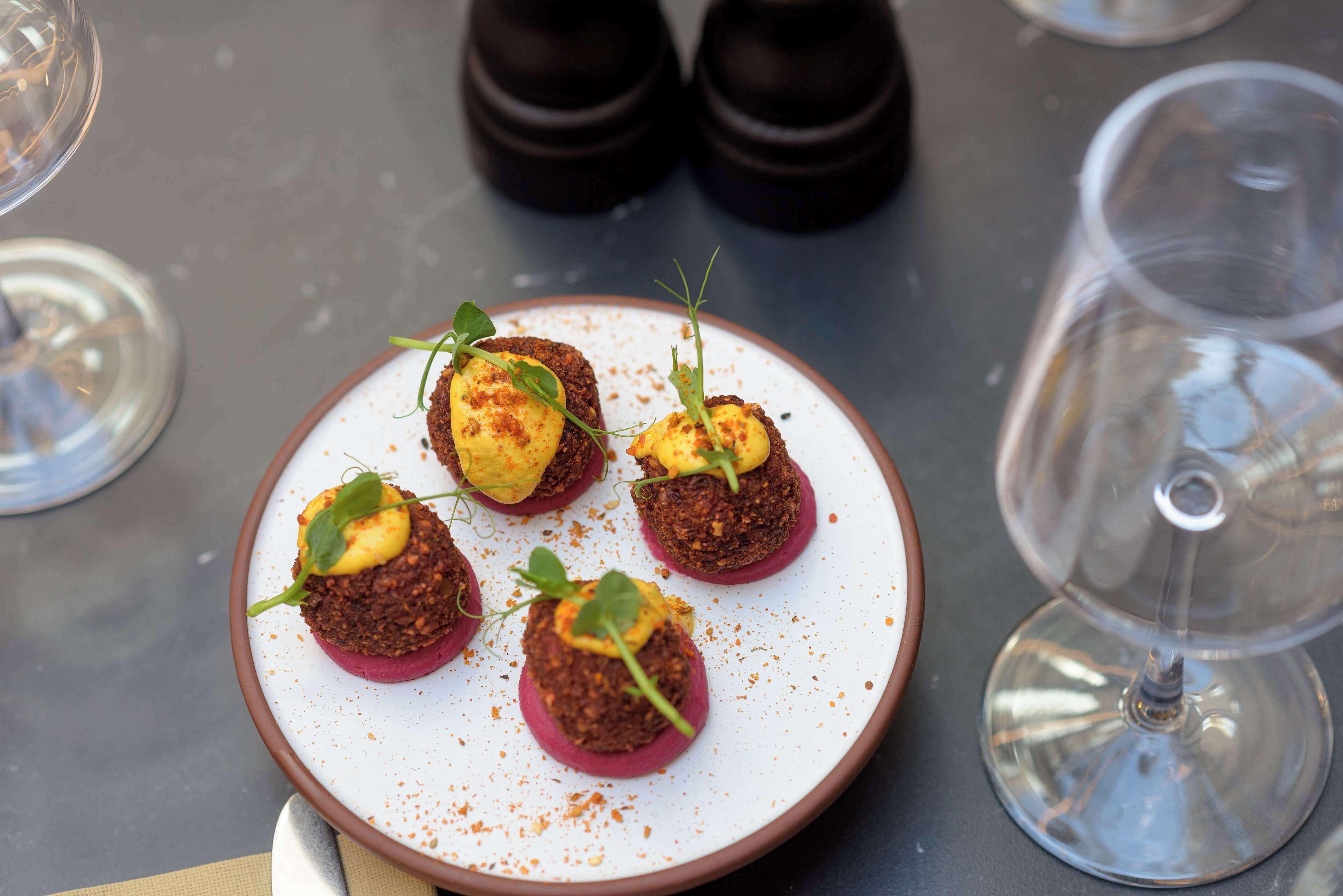 A plate of food with a white rim and a brown edge, accompanied by a wine glass and salt and pepper shakers.