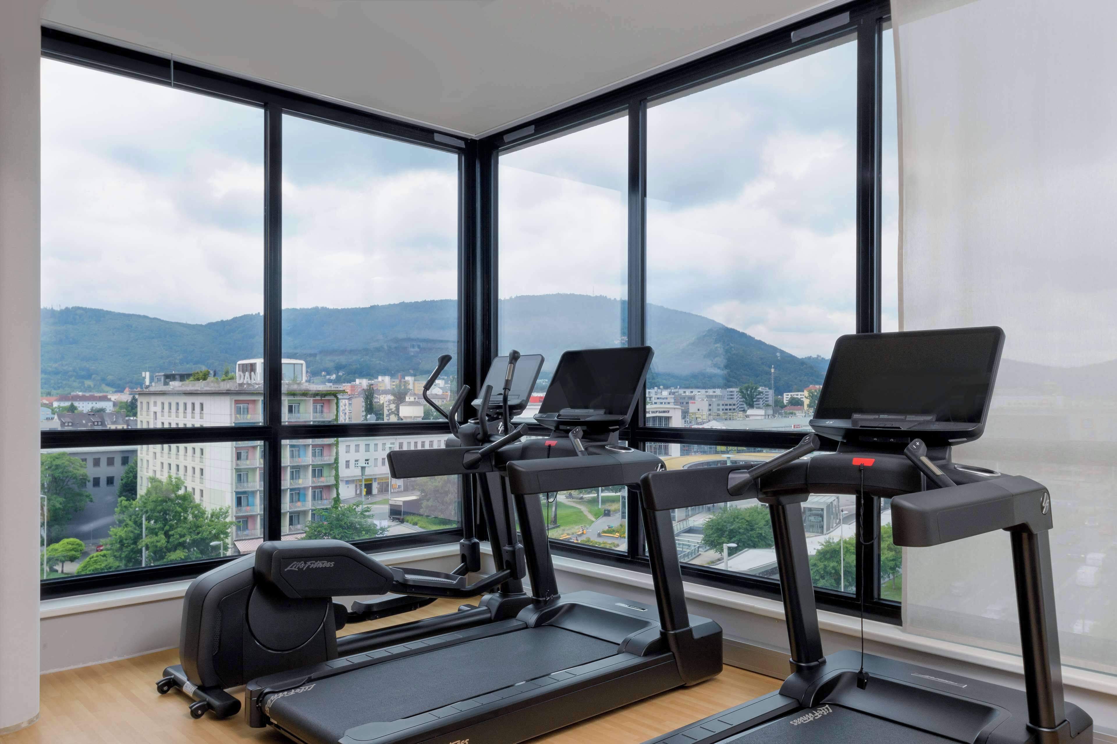 A gym with exercise equipment and a large window offering a city view.