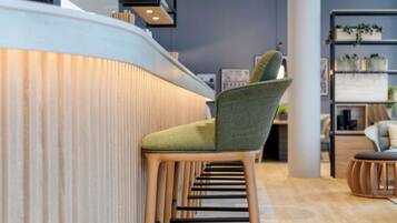 A modern bar area with a green upholstered bar stool, wooden counter, and shelves with plants.