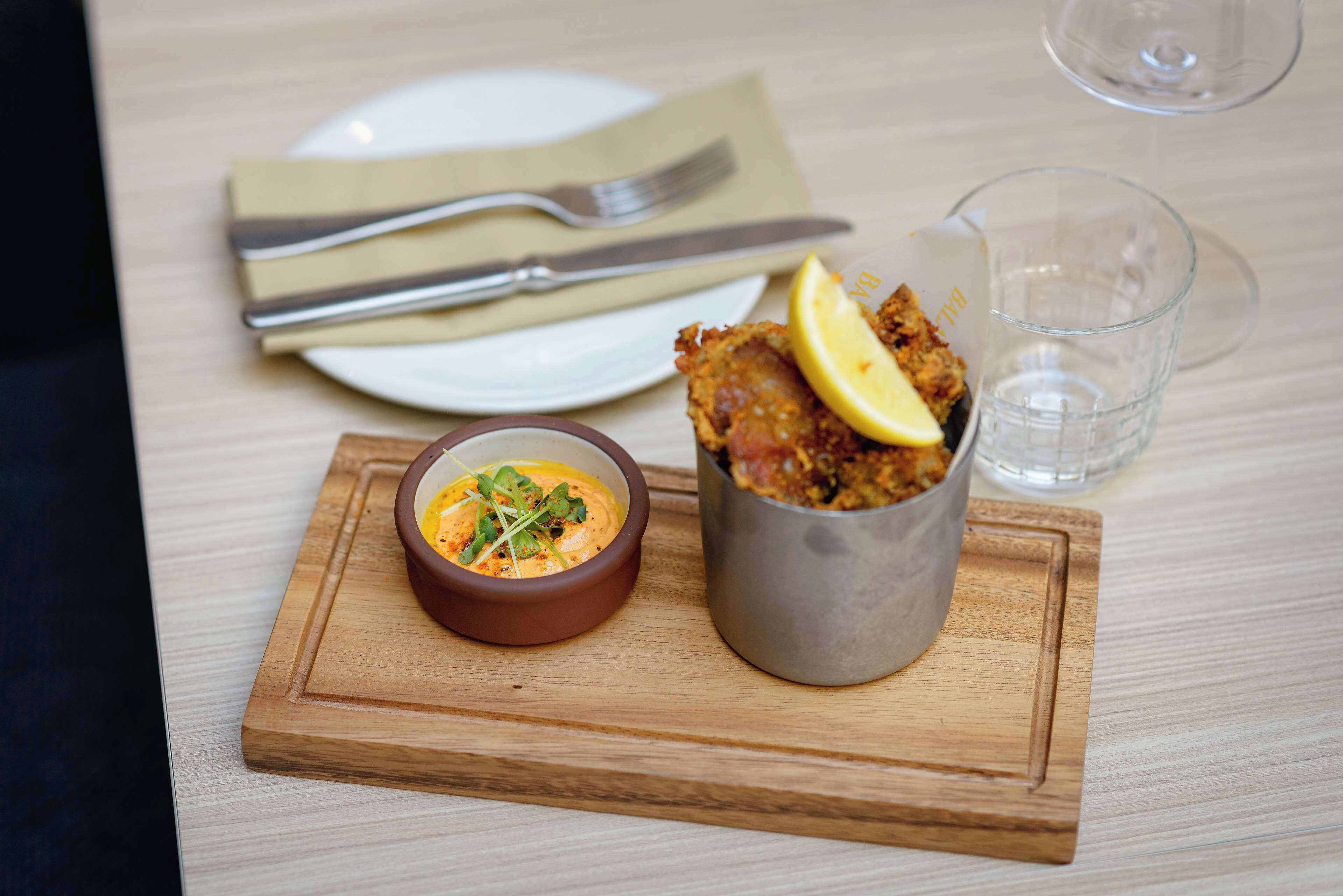 Un plato con una rodaja de limón, un recipiente de salsa y un vaso de agua sobre una tabla de madera.