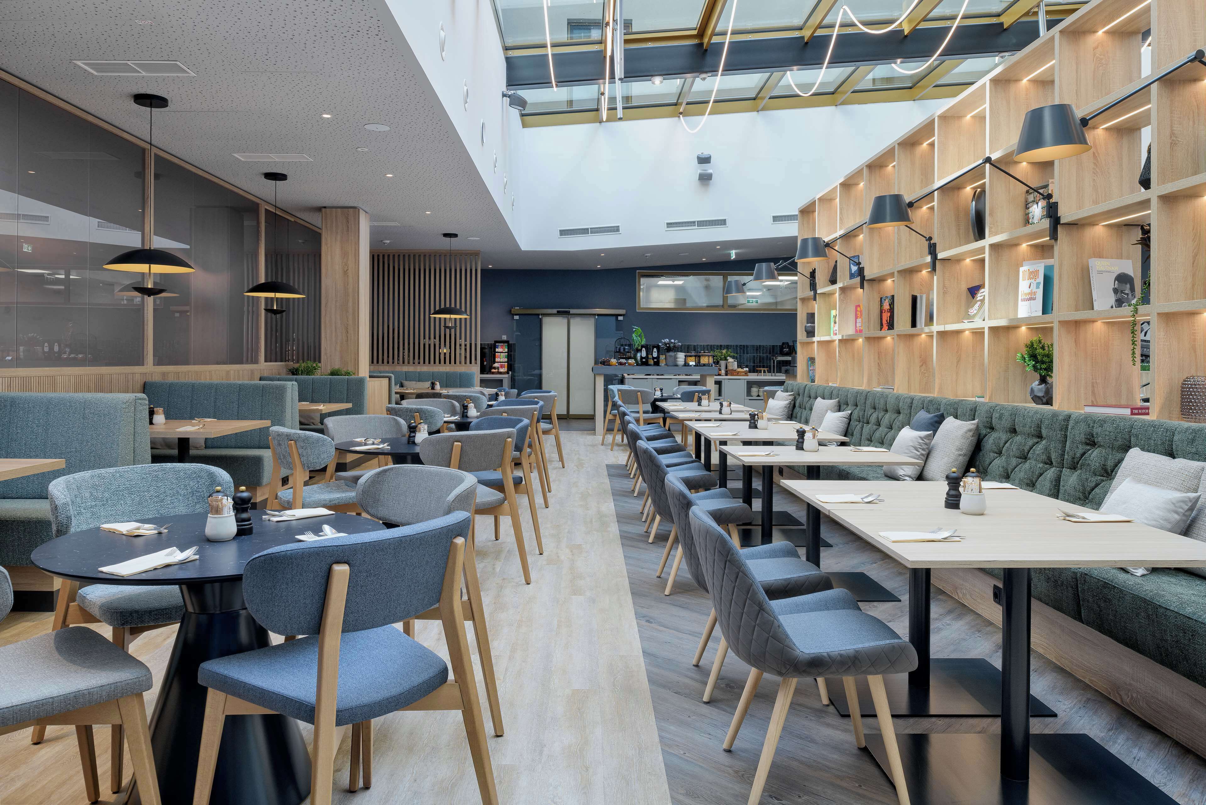 A modern restaurant with high ceilings, natural light, and a mix of seating options including tables and booths.