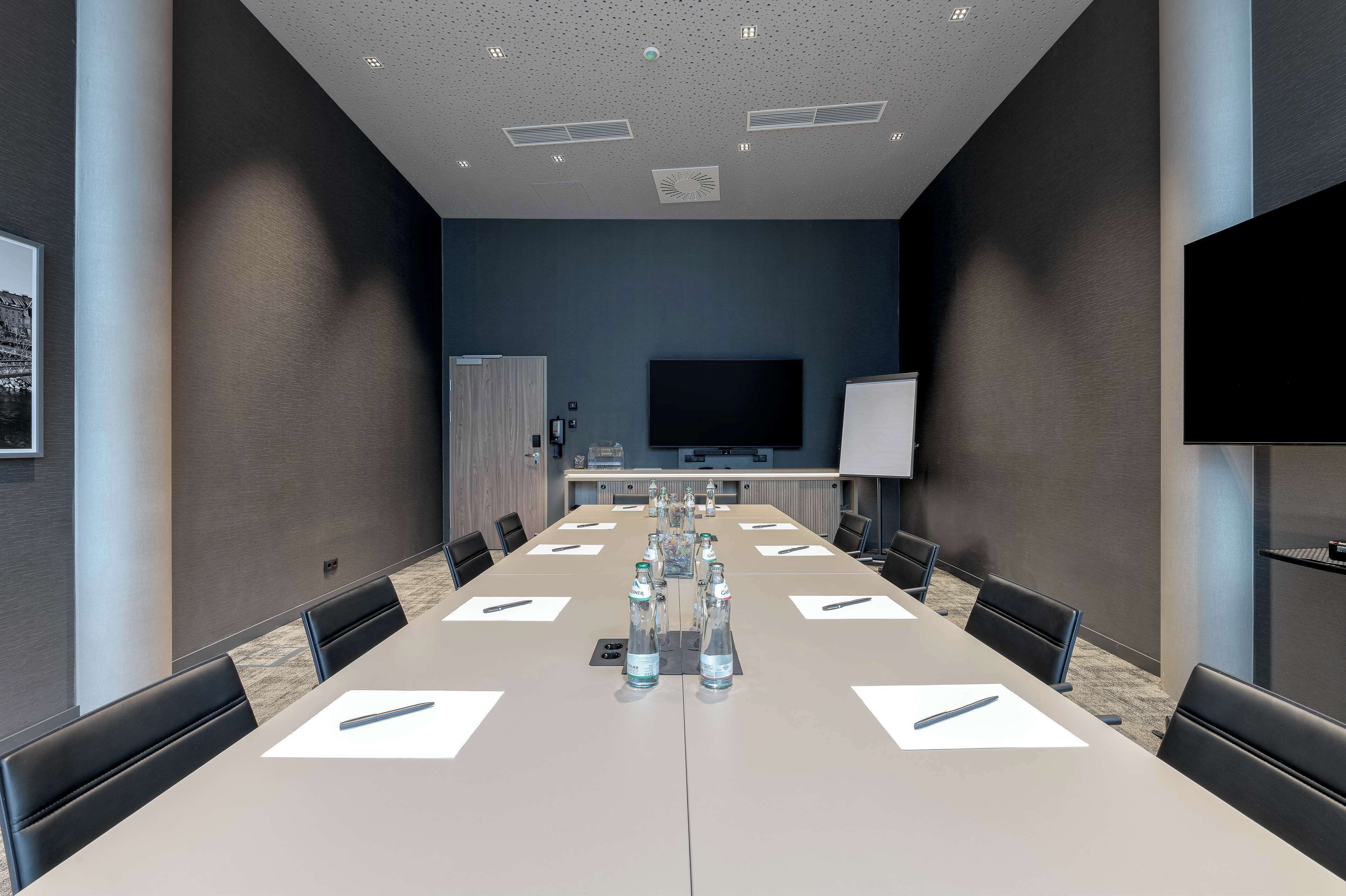 Une salle de conférence équipée d’une longue table, de chaises, d’un téléviseur et d’un tableau blanc.