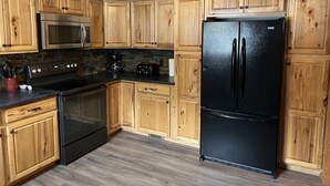 A kitchen with wooden cabinets, a black refrigerator, a microwave, and an oven. - Newly renovated, only 2 miles from downtown Fort Kent.  Right across from trails (Fort Kent)