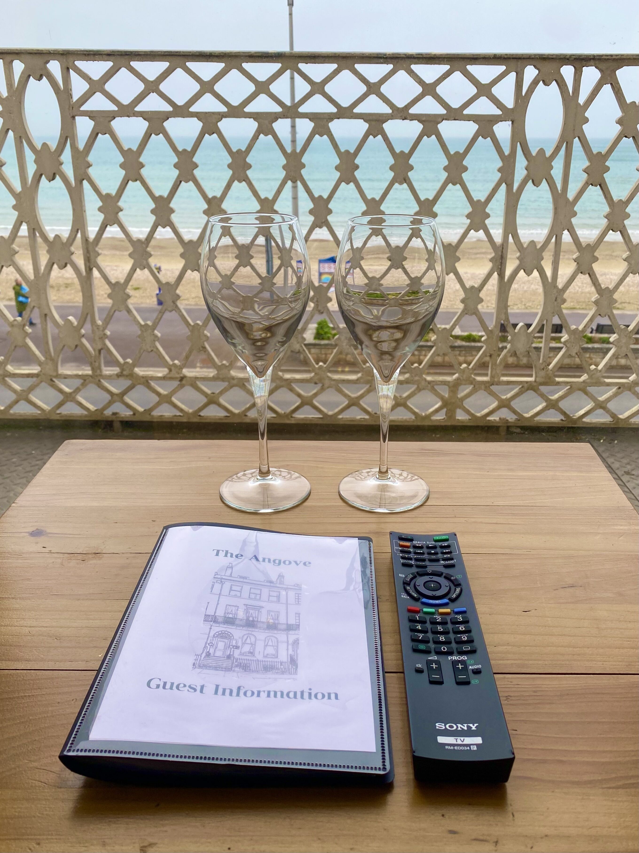 Two empty wine glasses on a wooden table with a remote control and a guest information booklet.