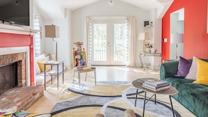 A spacious living room with a fireplace, a green sofa, a colorful rug, and a large window with curtains. - Spacious 4BD Country Gem - Fire Pit & Chill Vibes (Highland)