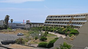 A hotel with a modern design, featuring a large building with multiple balconies and a parking area with a few cars.