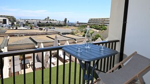 A balcony with a table and chairs, overlooking a landscaped area with a pool and buildings in the background.