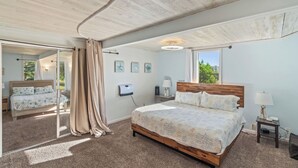 A bedroom with a wooden bed, a large window, and a ceiling with exposed beams. - Beachfront Cabin, Downtown, Hot Tub, Fully Fenced! (Ocean Shores)