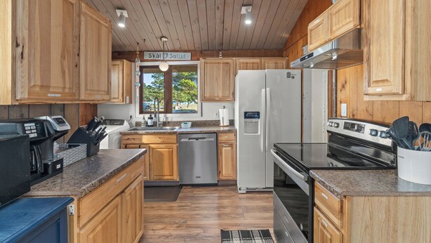 A modern kitchen with wooden cabinets, a stainless steel refrigerator, a built-in oven, and a granite countertop. - Beachfront Cabin, Downtown, Hot Tub, Fully Fenced! (Ocean Shores)