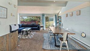 A modern living room with a sectional sofa, a dining table, and a grill. - Beachfront Cabin, Downtown, Hot Tub, Fully Fenced! (Ocean Shores)