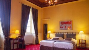 A hotel room with a double bed, two bedside tables with lamps, a red carpet, and a chandelier. - Château le Haget (Montesquiou)