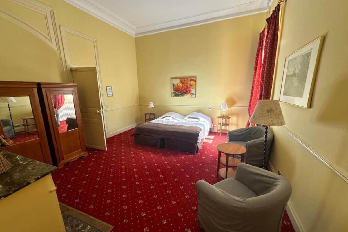 A hotel room with a bed, a chair, a small table, and a wardrobe.