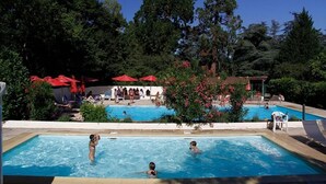 A swimming pool area with multiple pools, surrounded by lush greenery and red umbrellas. - Château le Haget (Montesquiou)