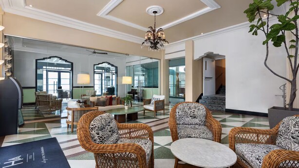A spacious lobby with wicker furniture, a chandelier, and a large mirror reflecting the room. - Roami at Hotel Astor (Miami Beach)