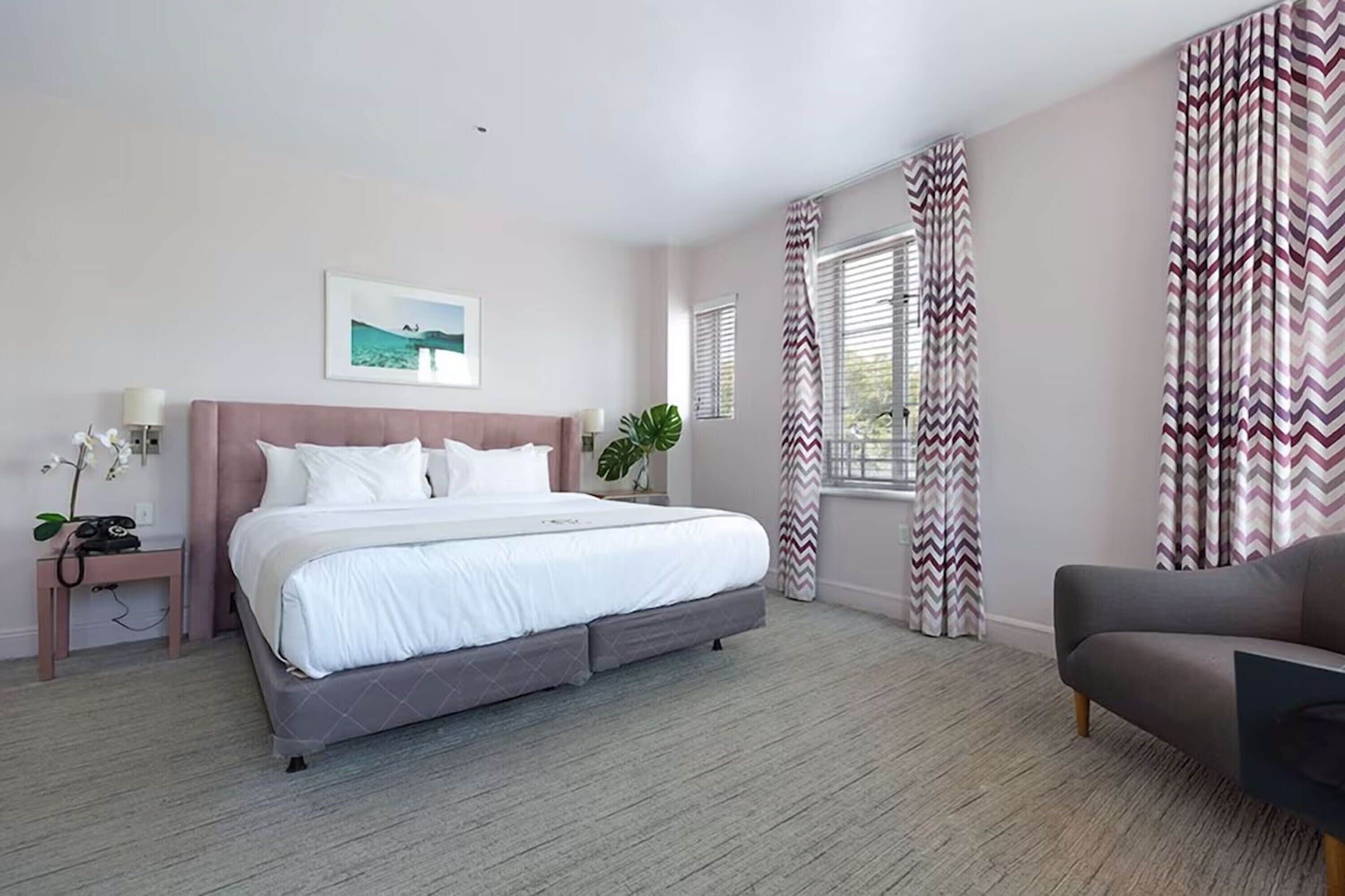A bedroom with a bed, bedside table, lamp, and curtains.