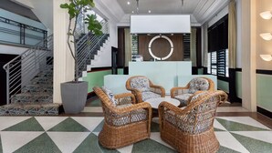 A lobby with wicker furniture, a staircase, and a reception desk. - Roami at Hotel Astor (Miami Beach)