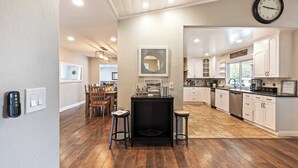 A modern kitchen with wooden flooring, a black island, and white cabinetry. - Breathtaking Meadows by Avantstay Temecula Group Retreat Pool, Pickleball, Firepit, Hot Tub (Temecula)