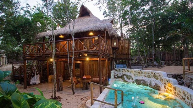 Une structure en bois avec un toit de chaume, une piscine et un espace salon extérieur.