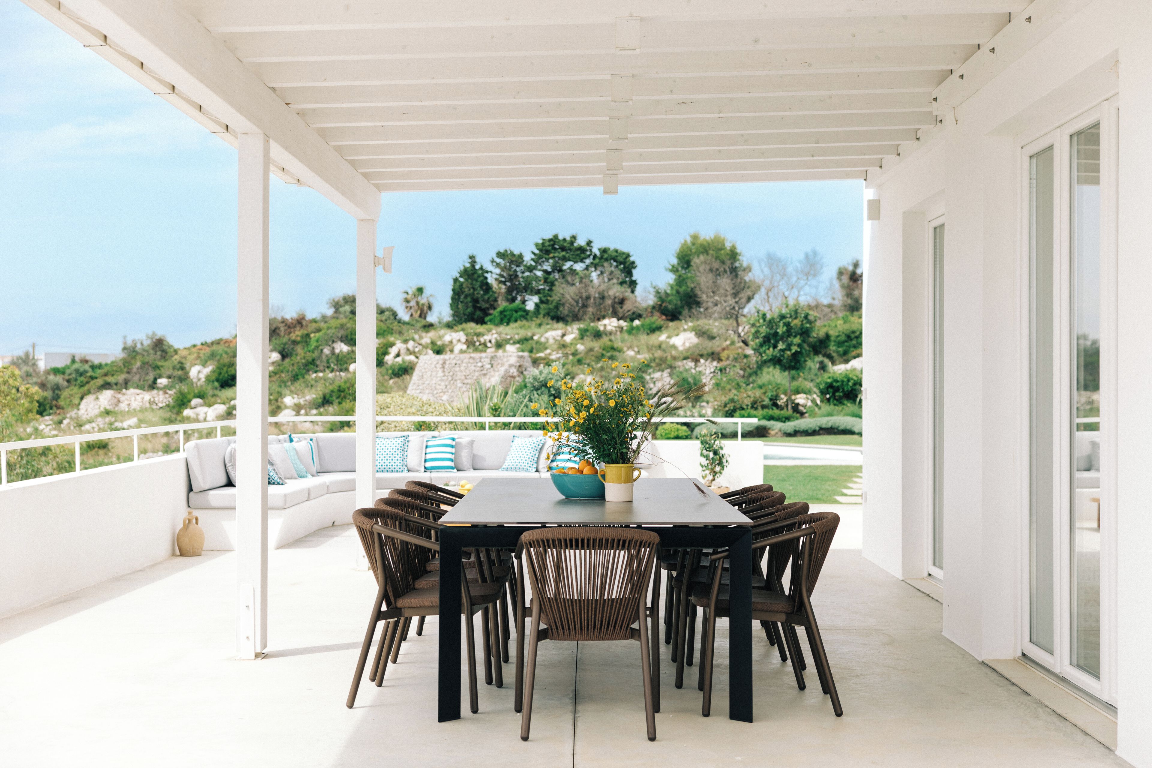 An outdoor patio with a round table and chairs, a white ceiling, and a view of a natural landscape.
