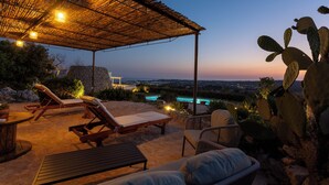 Une terrasse extérieure avec des chaises longues, une table et un espace abrité éclairé.