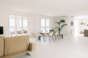 A modern living room with a sofa, dining area with chairs, and a large window with a view. - Luxury Villa Leucade, between sky and sea (Santa Maria di Leuca)