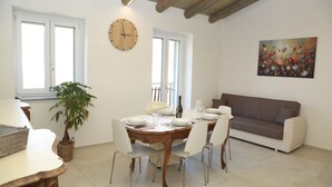 Un coin repas avec une table ronde dressée pour quatre personnes, entourée de chaises blanches, d’une plante en pot et d’un canapé marron.