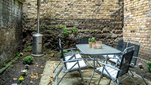 Een bakstenen muur met een metalen tafel en stoelen, een afvalbak en potplanten.