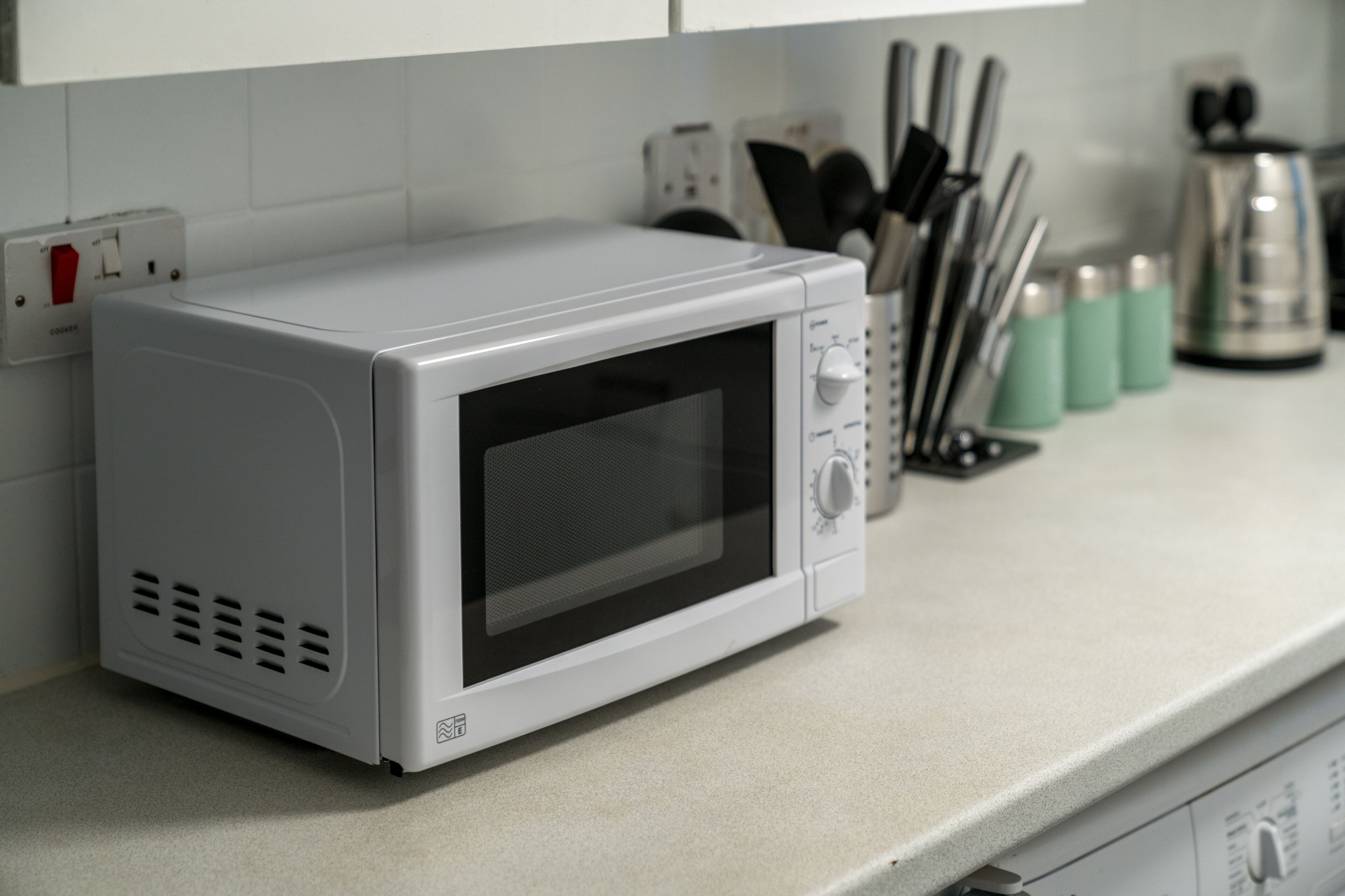 A white microwave oven on a kitchen counter with a white tiled backsplash.