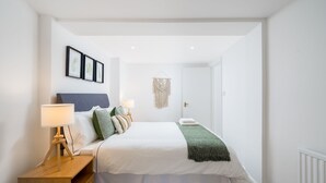 Een keurig opgemaakt slaapkamer met een bed, nachtkastjes en een macramé wanddecoratie.