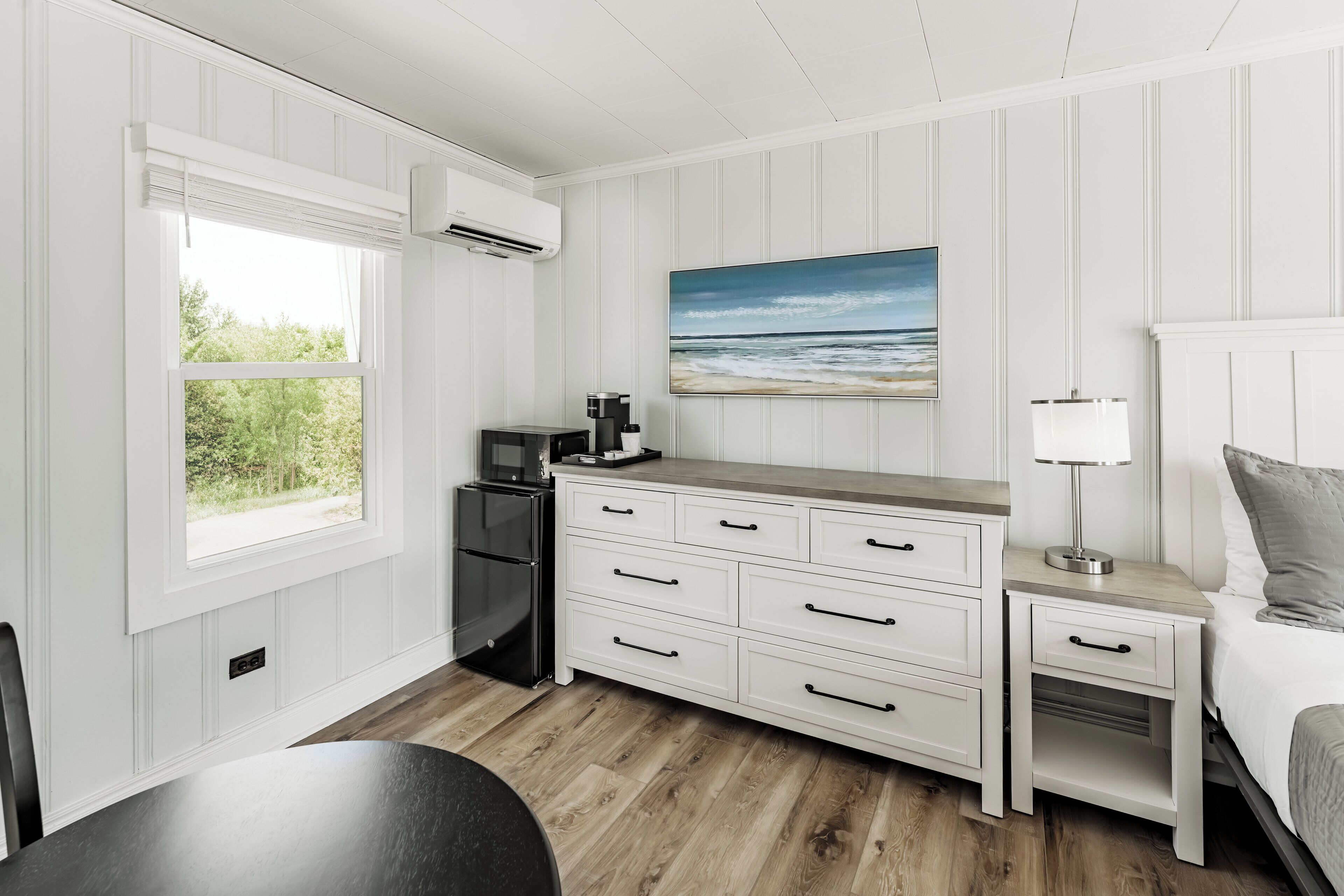 A compact bedroom with a bed, bedside table, and a painting of a beach scene.