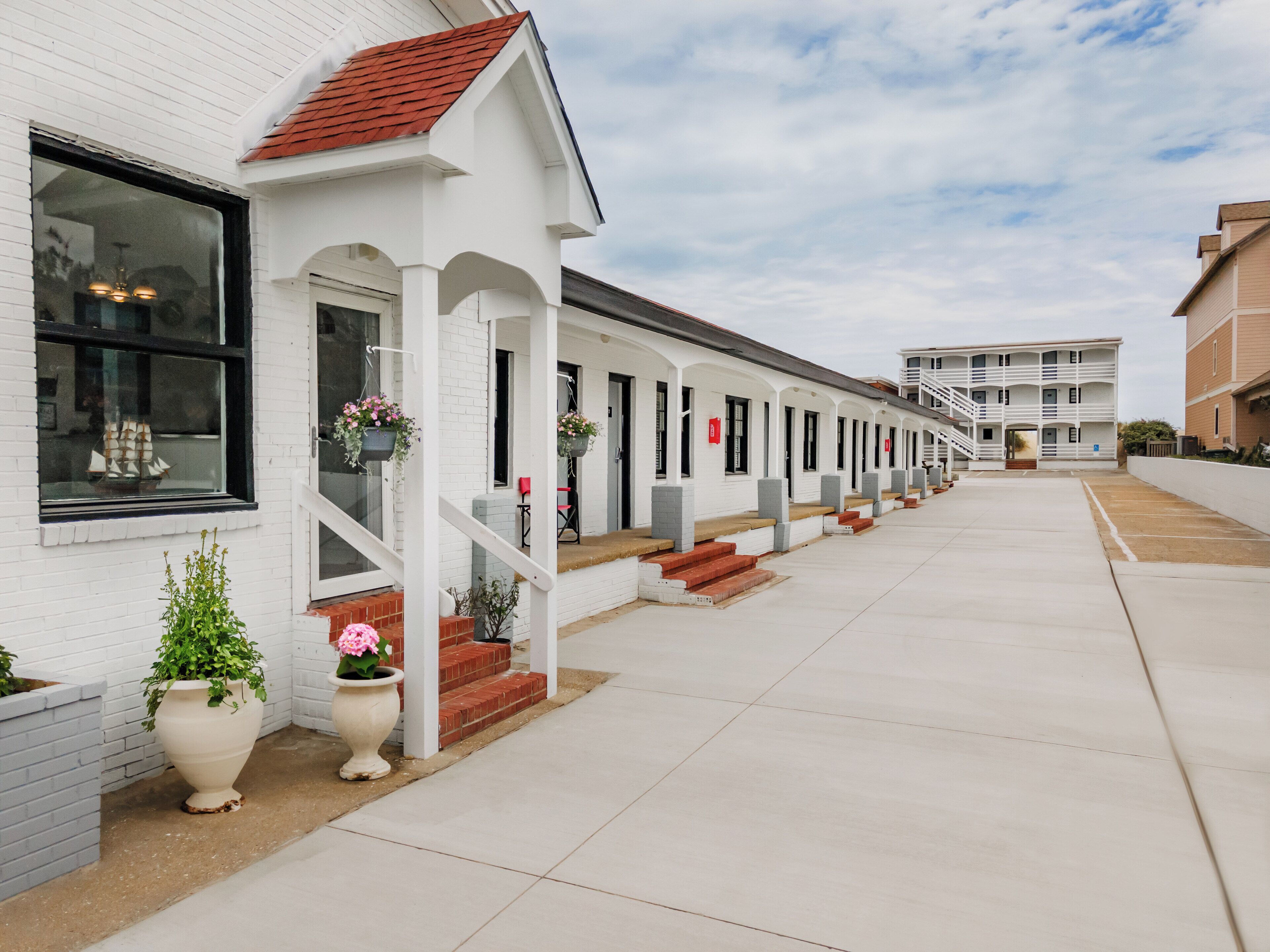 A row of white buildings with red roofs, each featuring a small porch with steps leading up to the entrance.