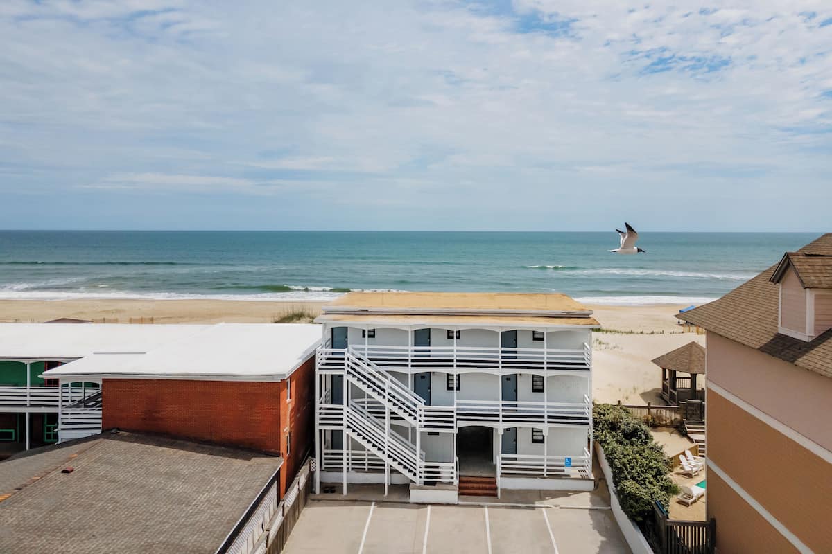 A beachfront hotel with a white exterior, a staircase leading to the entrance, and a view of the ocean.
