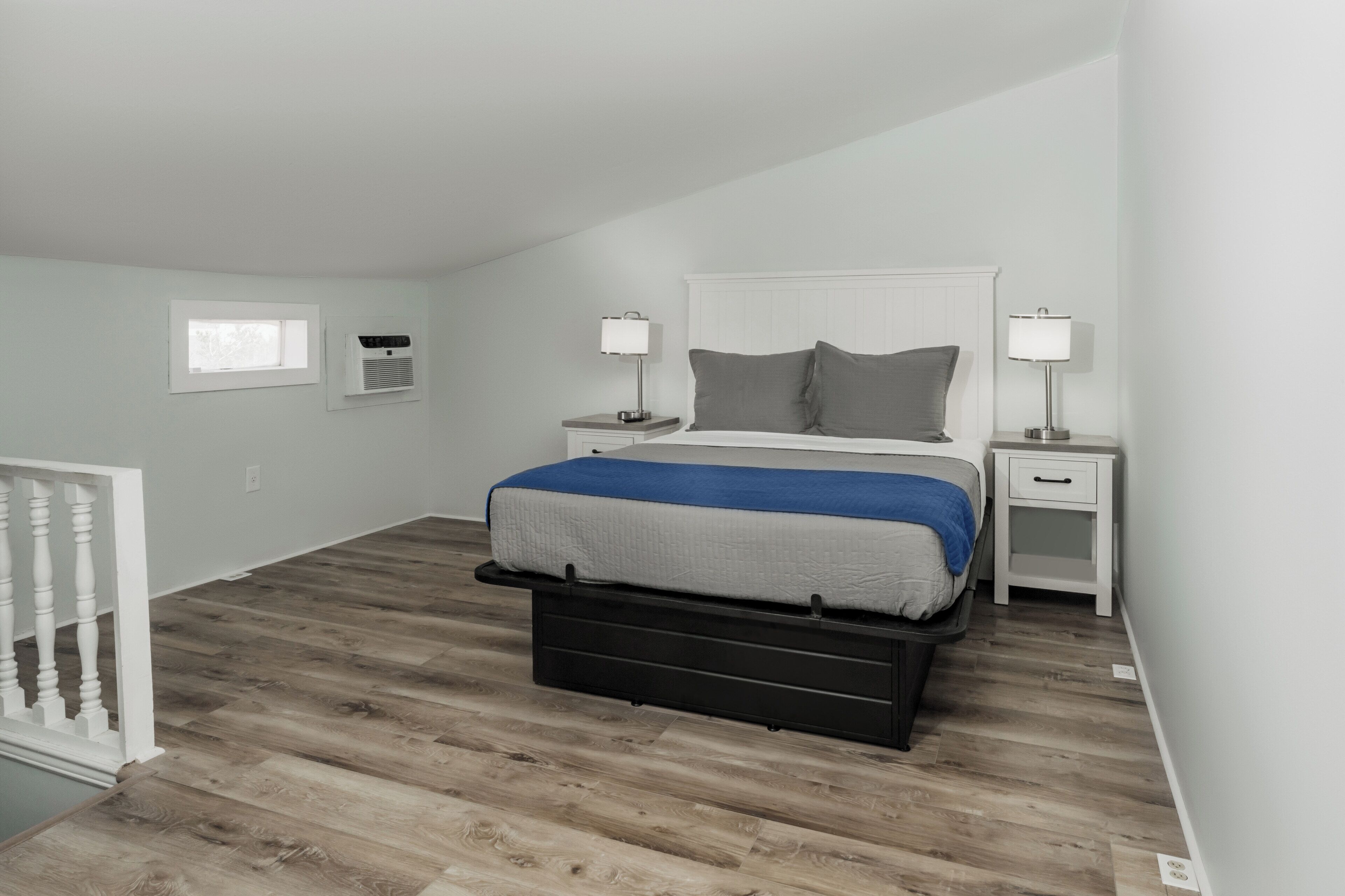 Un dormitorio con cama, mesitas de noche, una ventana y una barandilla blanca.