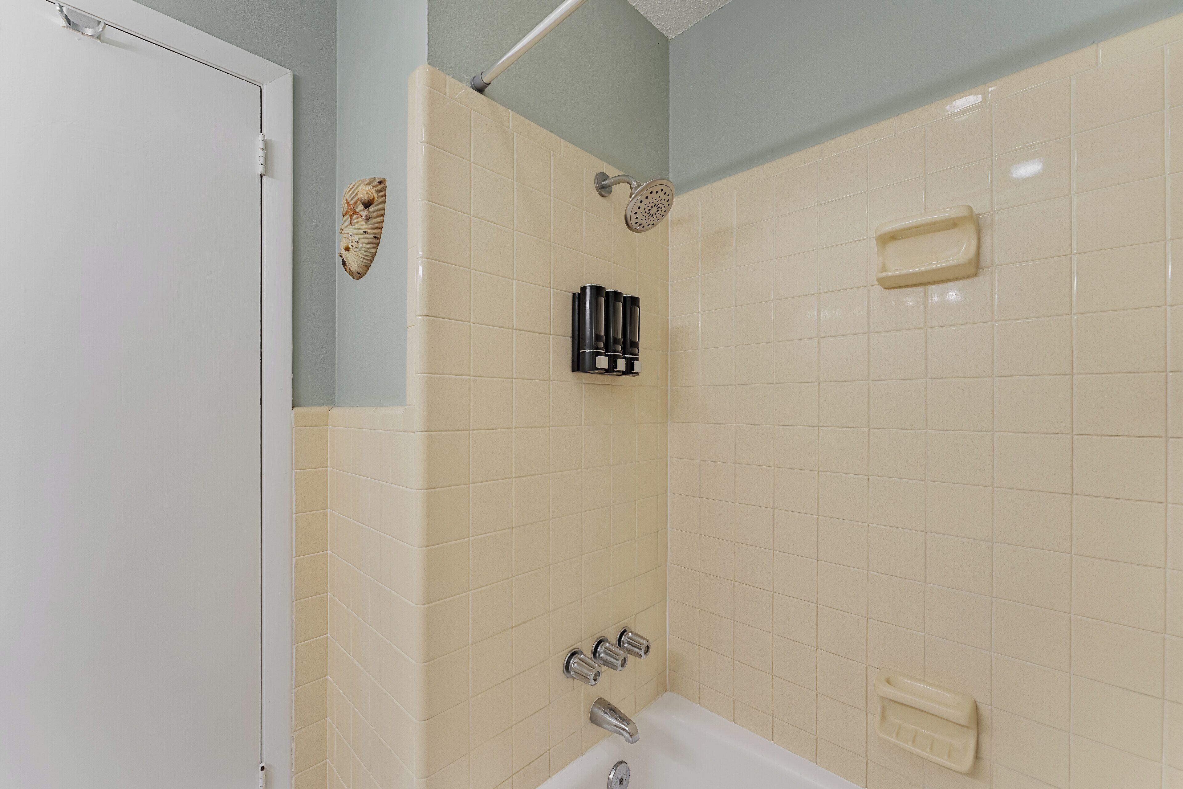 A bathroom with beige tiles, a white bathtub, a showerhead, and a soap dish.