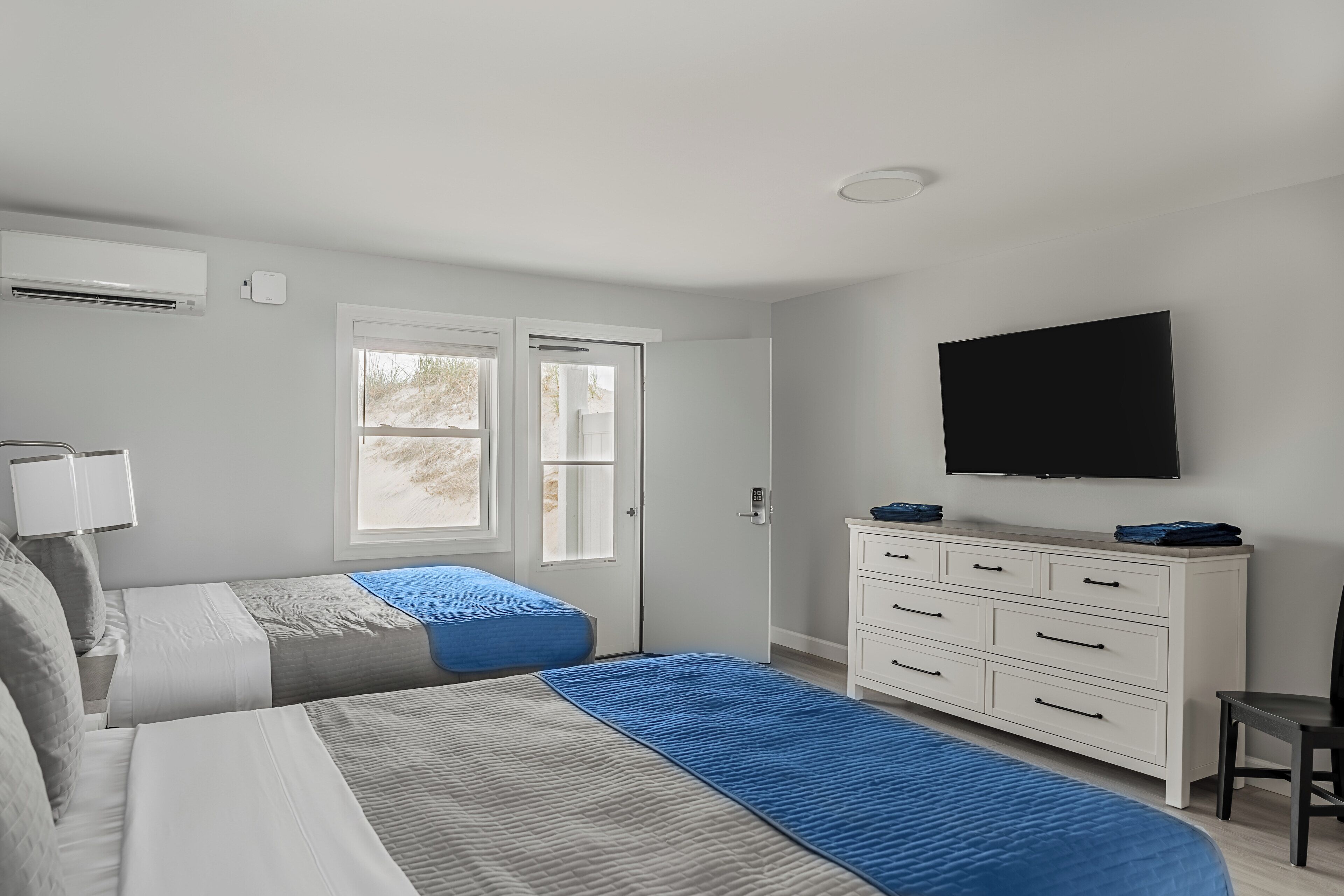 A bedroom with two beds, a TV, a dresser, and a window.