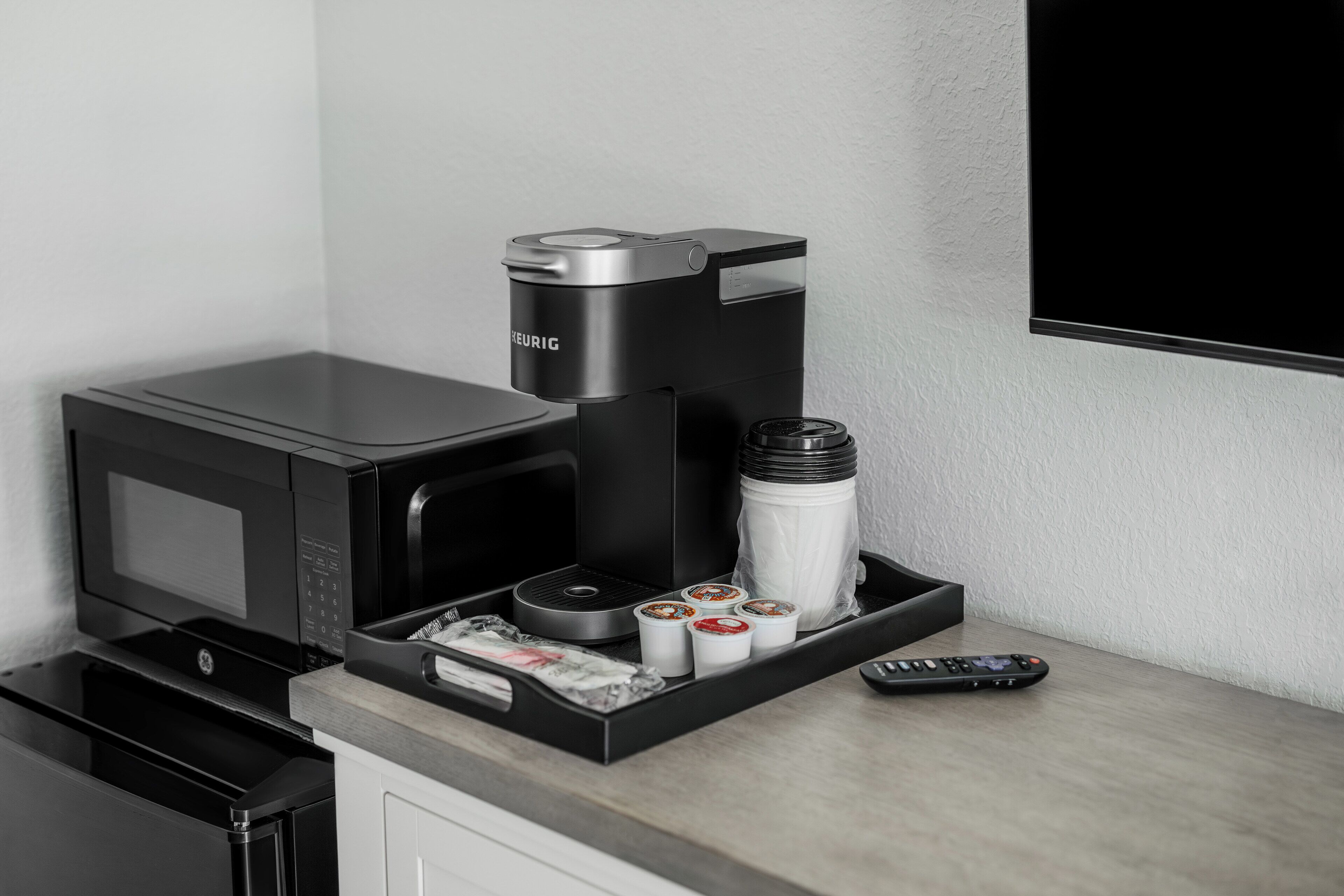 A kitchenette with a Keurig coffee maker, a microwave, a water dispenser, and a remote control.