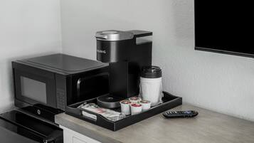 Una kitchenette equipada con una cafetera Keurig, un microondas, un dispensador de agua y un control remoto.