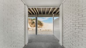 Un couloir aux murs en briques blanches et au sol en béton, qui mène à un point de vue sur la plage.
