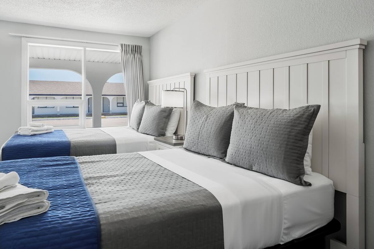 A hotel room with two beds, a large window with a view, and a balcony.