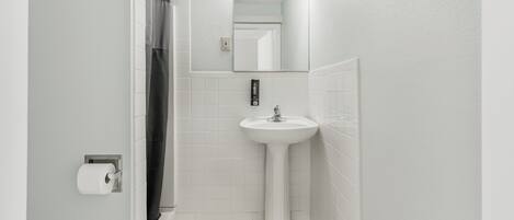 A bathroom with a white sink, a mirror with lights, and a shower curtain.