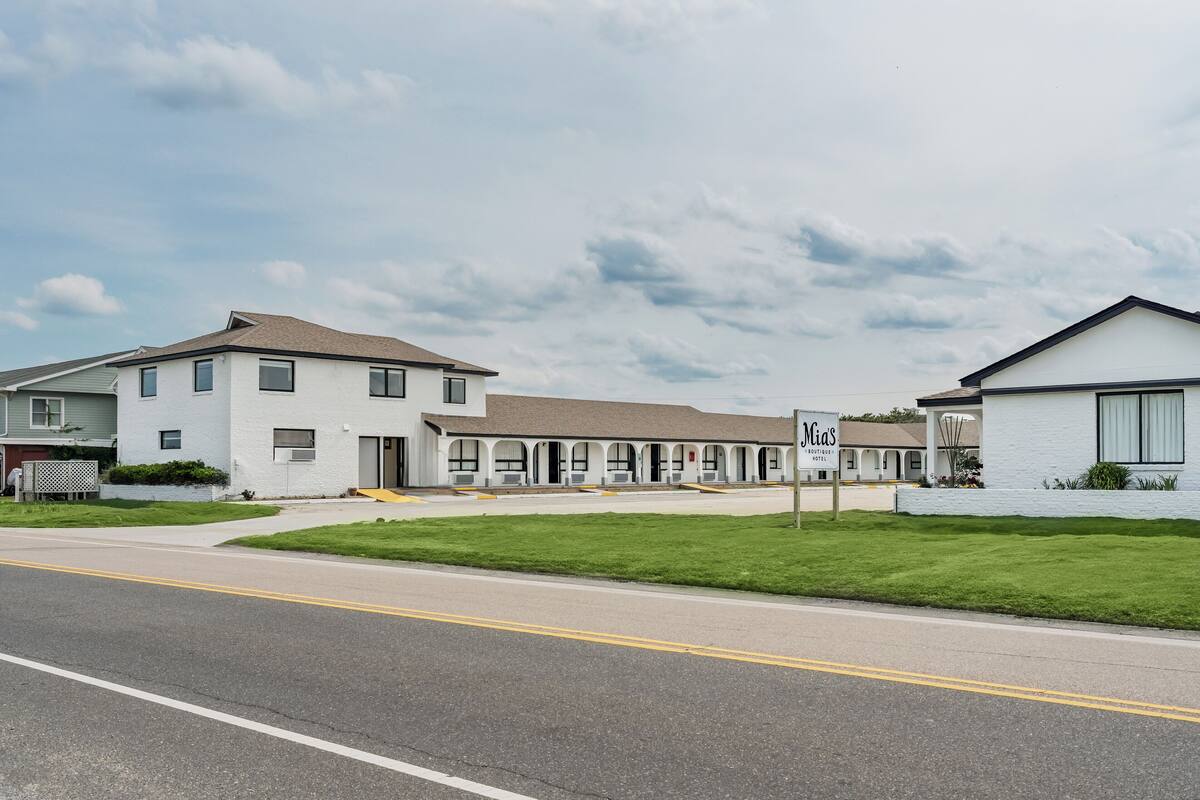 A motel with a row of single-story buildings, each with a front porch and a sign indicating the name.