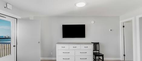 A room with a white dresser, a flat-screen TV mounted on the wall, a chair, and a bed with a blue bedspread.