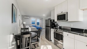 Une cuisine moderne avec des meubles blancs, un réfrigérateur en acier inoxydable, un four à micro-ondes et une cuisinière. On y trouve également un coin repas avec une table et des chaises.