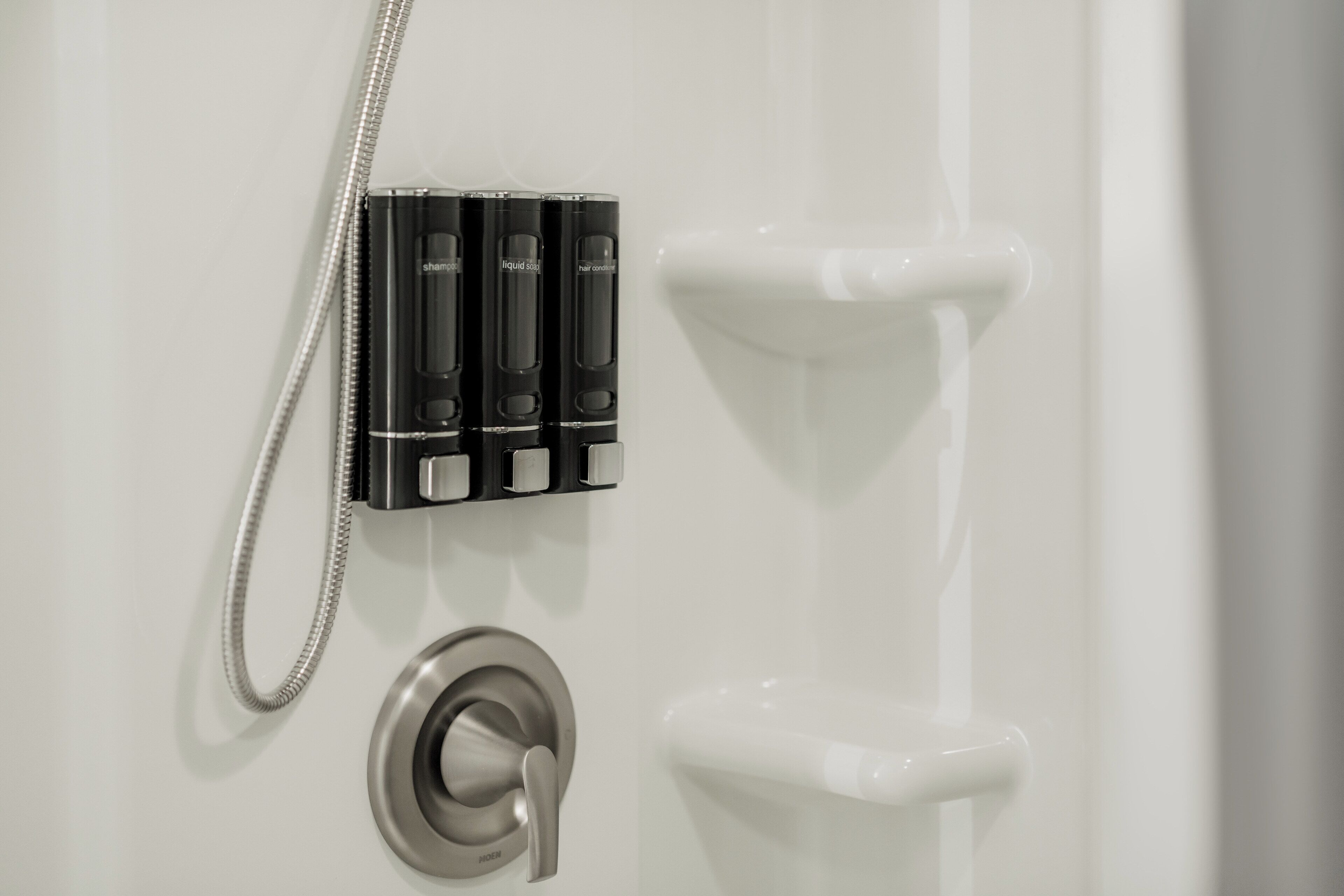 Un baño con ducha, botellas negras y un grifo plateado.